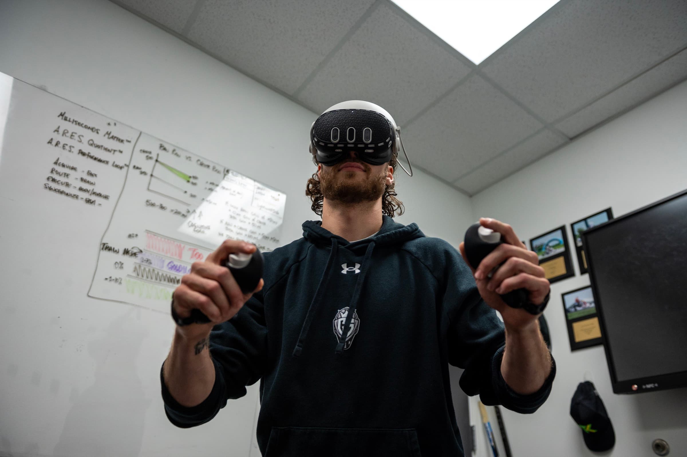 A goalie training in a VR headset beside the A.R.E.S. Performance Loop whiteboard