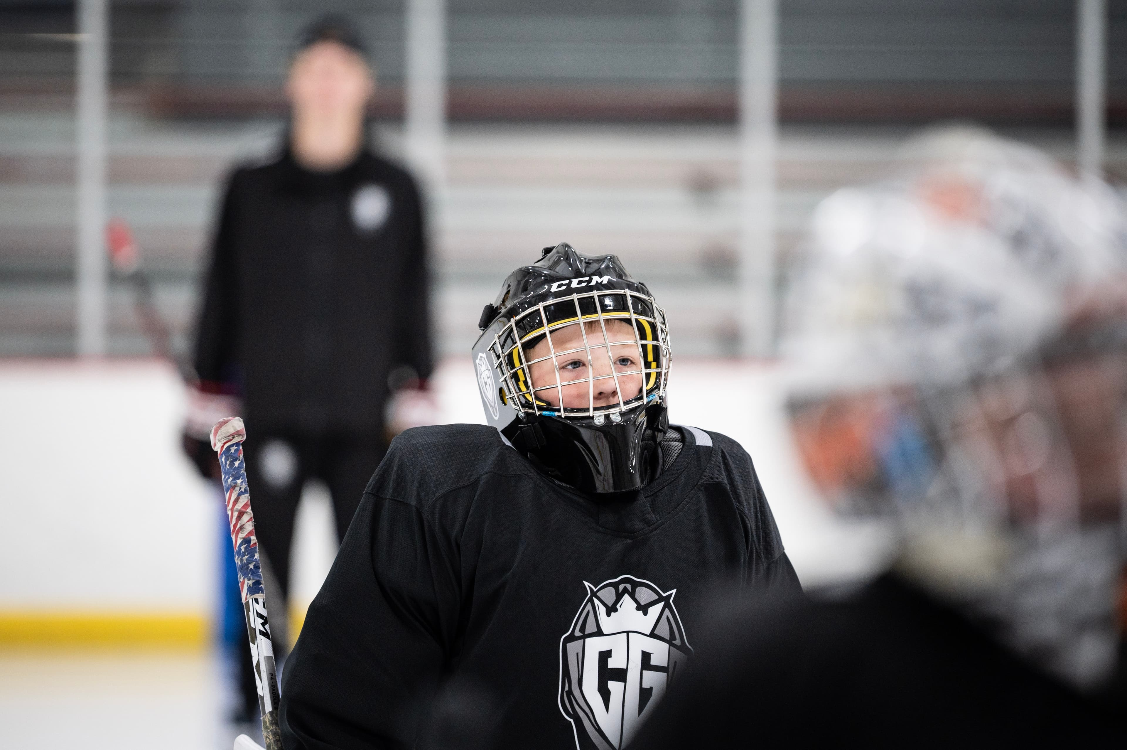 A young CGG goalie on the ice, a coach behind them.
